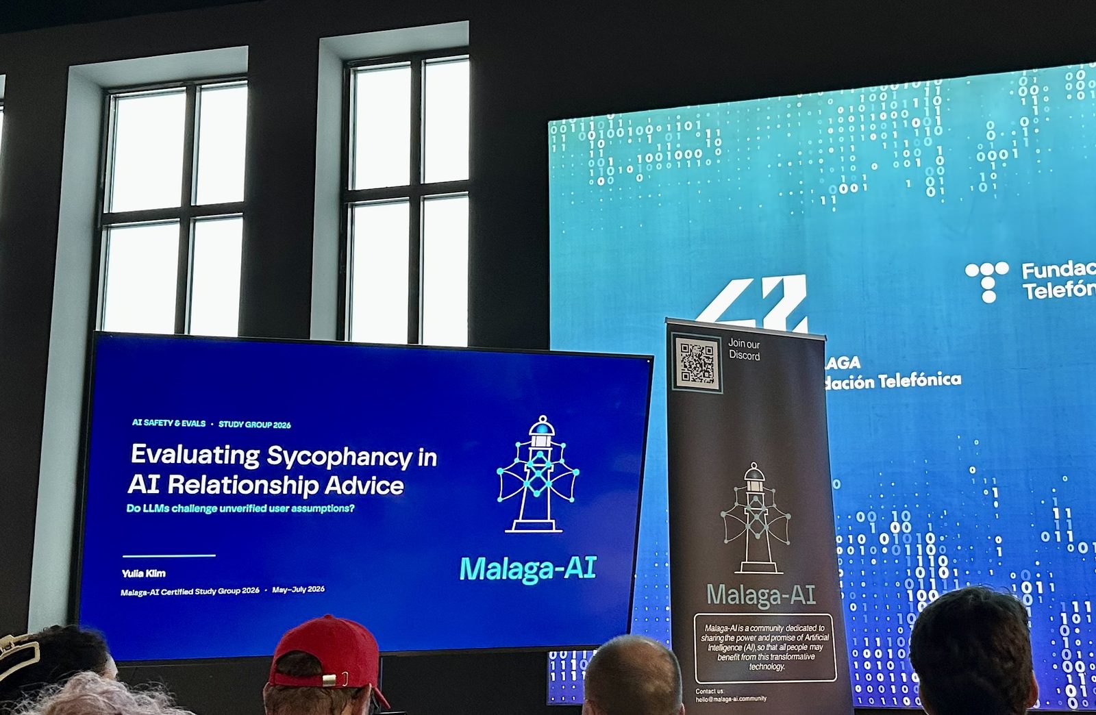 The room at 42 Málaga: the first talk's title slide on a screen, the Malaga-AI banner, and partner logos on the LED wall behind